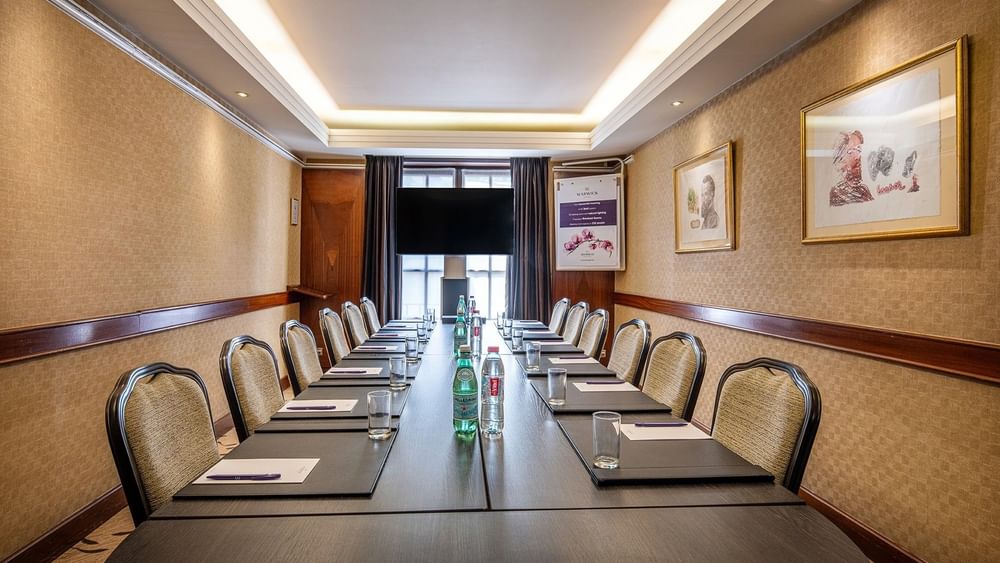 Ensor room setup with chairs and table facing hanging TV by the window at Warwick Grand-Place Brussels