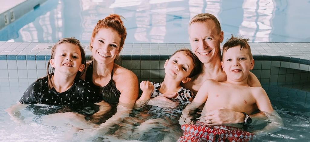 A smiling family of five enjoying time together in an indoor hotel pool, capturing a warm and relaxed atmosphere.