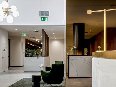 Modern BTR lobby with a marble reception desk, gold lamp, green armchair, and a decorative chandelier.