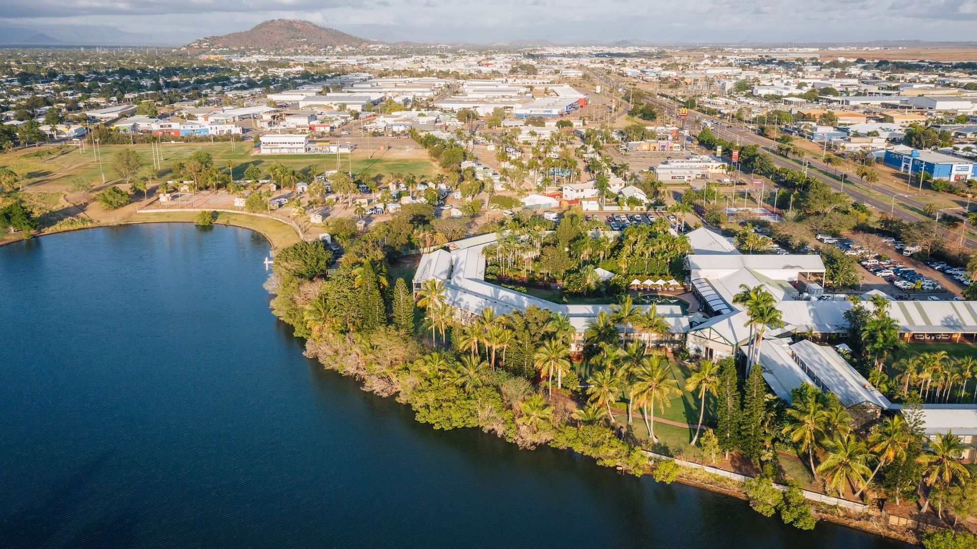 Aerial view of Mercure Hotel Townsville with a lake, palm trees against a mountain backdrop