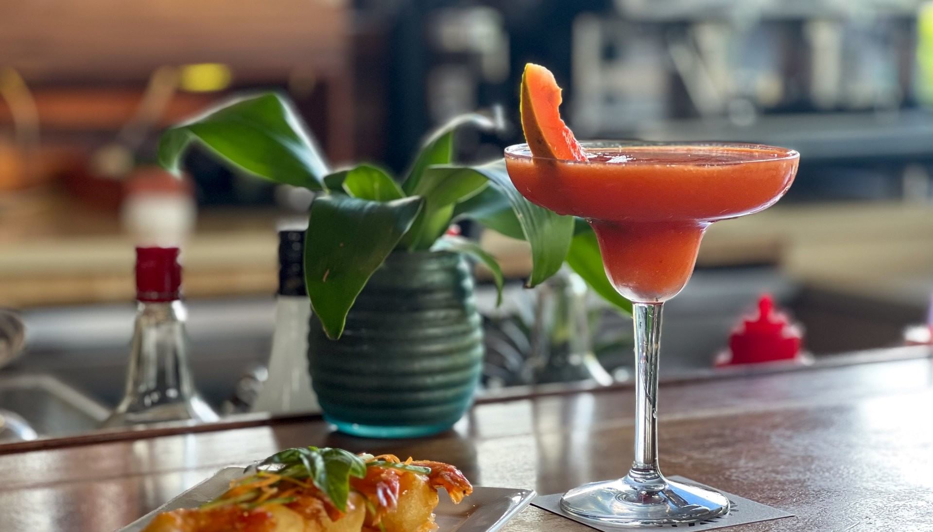 Plate of fried shrimp and a red cocktail by a small potted plant in KanaVata Restaurant at TokaToka Resort Nadi Fiji