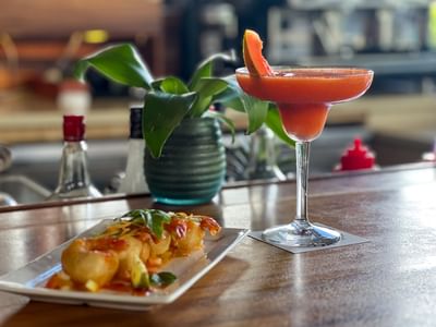 Plate of fried shrimp and a red cocktail by a small potted plant in KanaVata Restaurant at TokaToka Resort Nadi Fiji