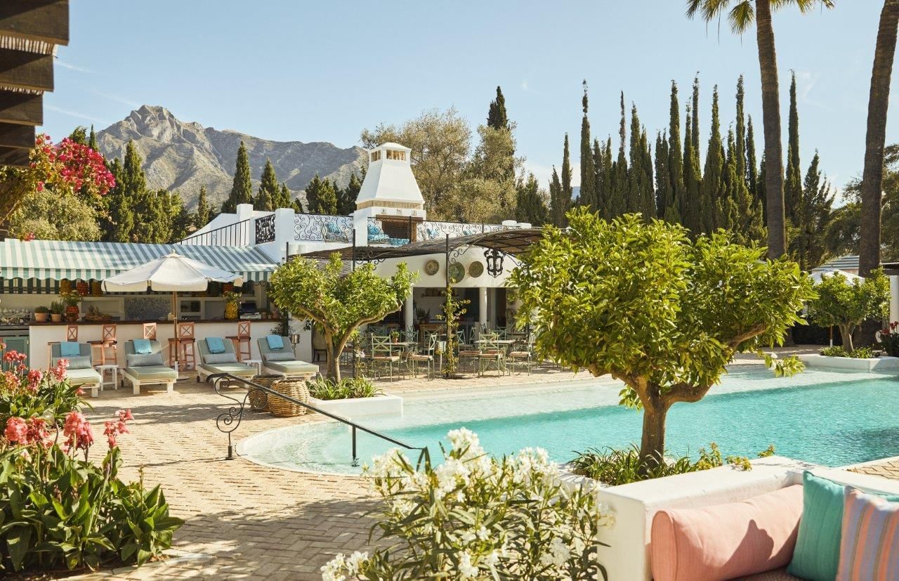 Sunny Marbella Club pool area with lounge chairs, bar, sun deck, and La Concha mountain in the background