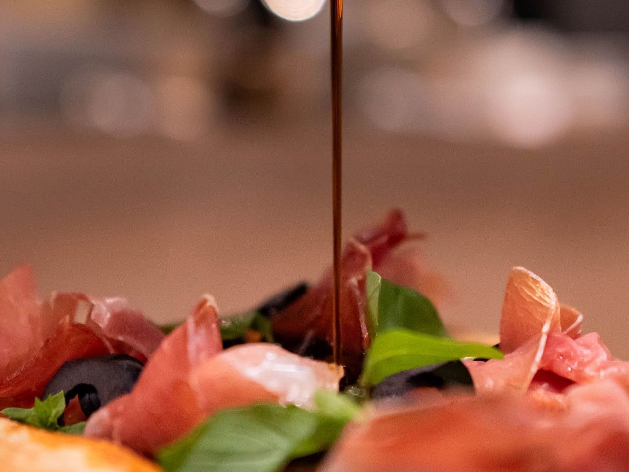 Se está echando aceite de oliva sobre una pizza con ingredientes en el hotel HCC Costanera Concepción.