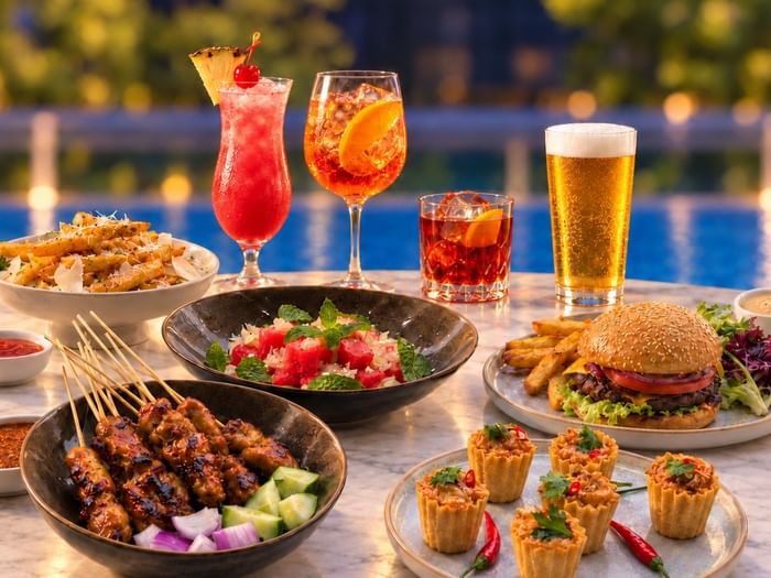 Colorful cocktails and beer alongside appetizers and a burger by a poolside setting for Sip & Chill