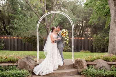 Newlywed couple kissing under a white archway in the garden at Lake Natoma Inn