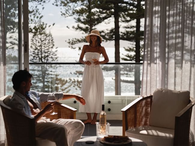 Couple relaxing on balcony with sea view, woman in hat holding wine glass at Elysium Hotels