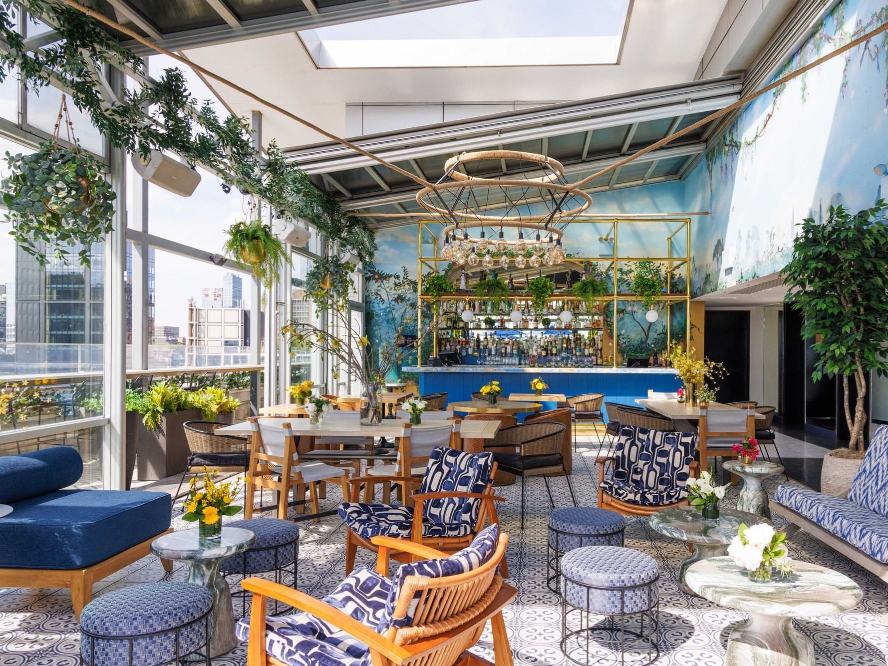 Modern, open-air lounge with blue and white seating, large glass windows, hanging plants, and decorative wall mural.