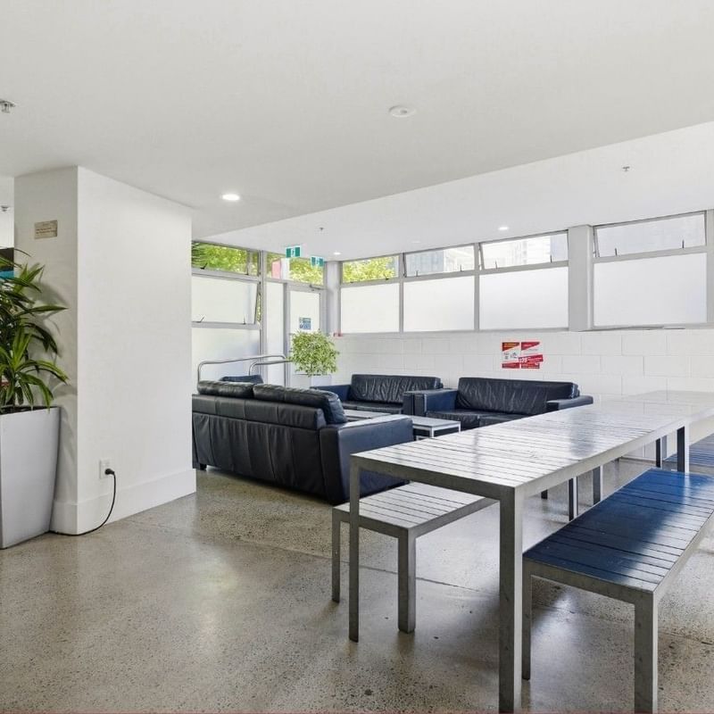 Modern lounge area with black couches, a large table, and a bookshelf at Student Living Auckland – Anzac.