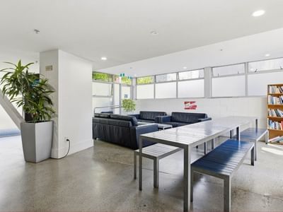 Modern lounge area with black couches, a large table, and a bookshelf at Student Living Auckland – Anzac.