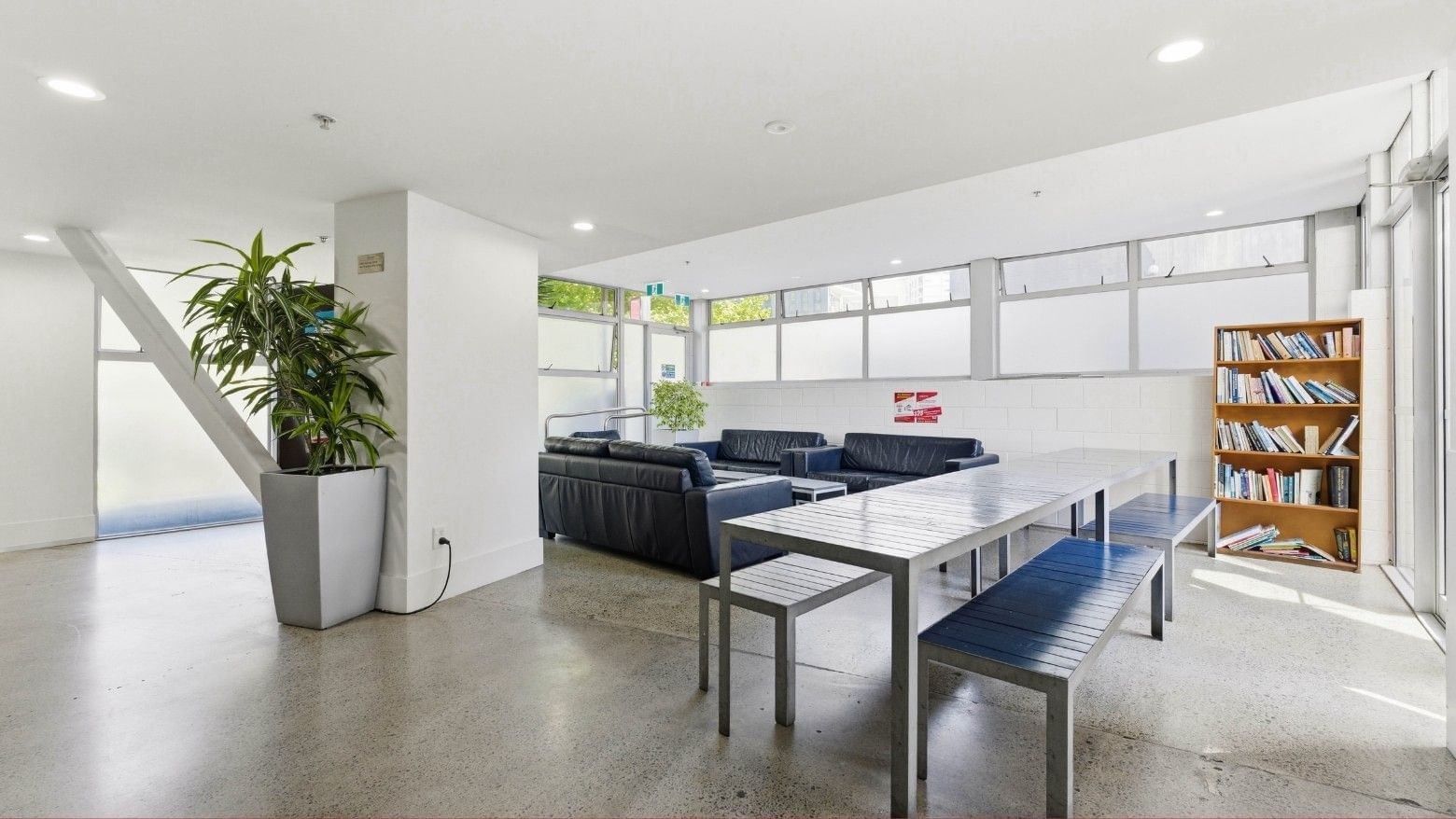 Modern lounge area with black couches, a large table, and a bookshelf at Student Living Auckland – Anzac.