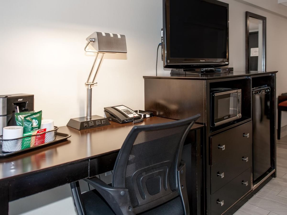 Desk with lamp, coffee maker, TV, and chair in a hotel room.
