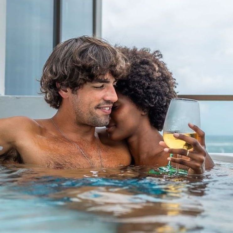Couple sharing a kiss in a hot tub with wine glasses in hand at Hibird