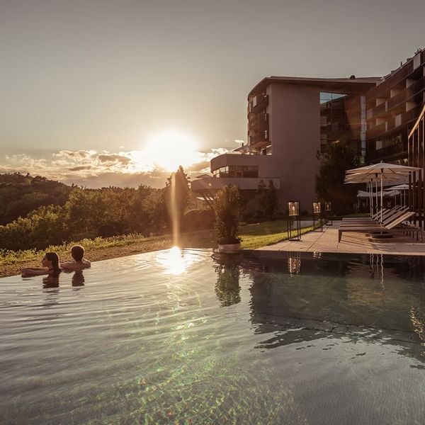 A couple relaxing in the pool by the deck at sunset in Falkensteiner Hotels & Residences