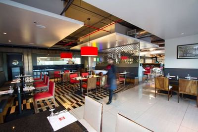 Restaurant with staff member by set dining tables and kitchen visible at D Sabana Hotel