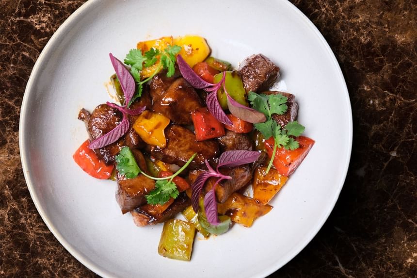 Dish of tender beef pieces sautéed with bell peppers, garnished with herbs & flowers in Square One at Park Hyatt Saigon