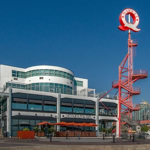 Exterior view of Coast Lonsdale Quay with a restaurant patio, red sculpture, and a boardwalk under a blue sky