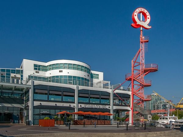 Exterior view of Coast Lonsdale Quay with a restaurant patio, red sculpture, and a boardwalk under a blue sky