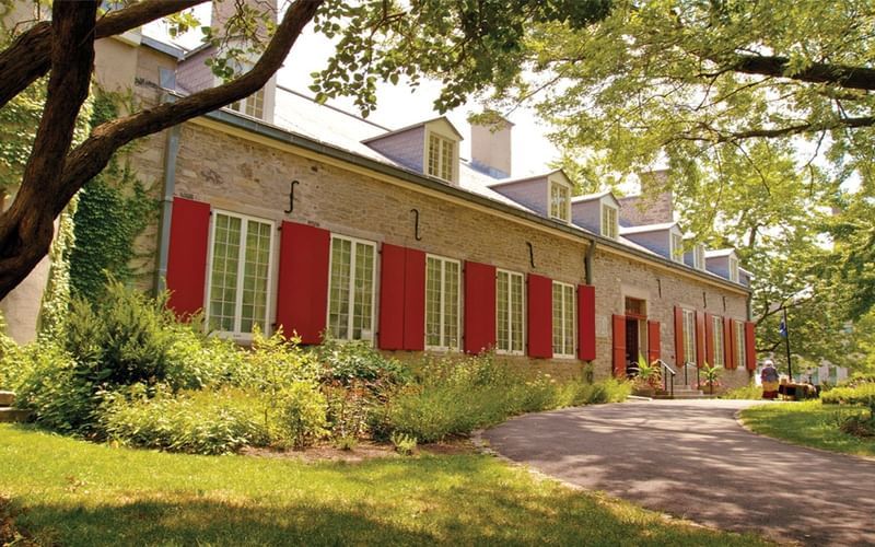 Historic stone building with red shutters surrounded by lush trees and green lawn at Warwick Le Crystal Montreal