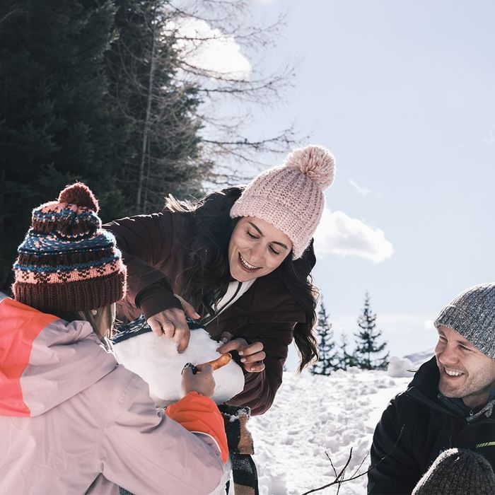 Familie baut im Schnee einen Schneemann, während sie fröhlich lacht und sich unterhält.