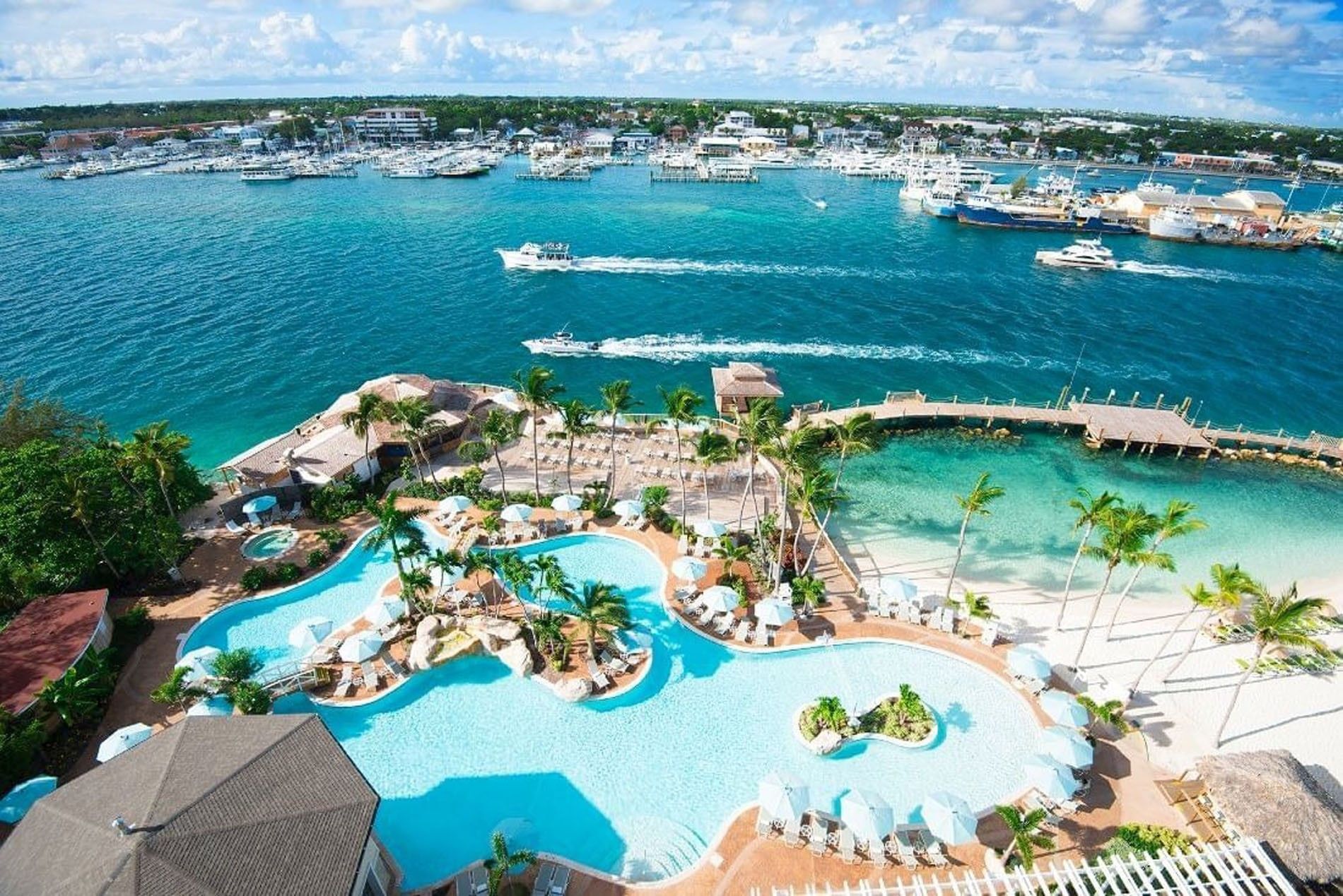 View of Warwick Paradise Island Bahamas, large pool by white umbrellas under palm trees surrounding a tropical harbor