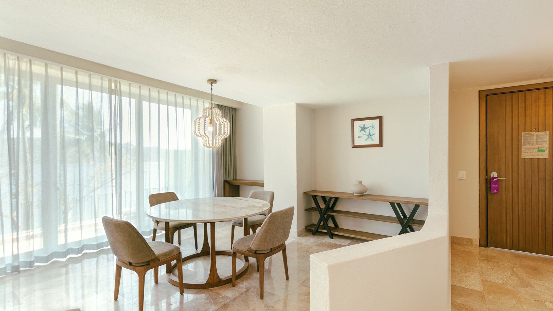 King Junior Suite dining area with a round marble table, wooden console, and beaded light at Camino Real Acapulco Diamante