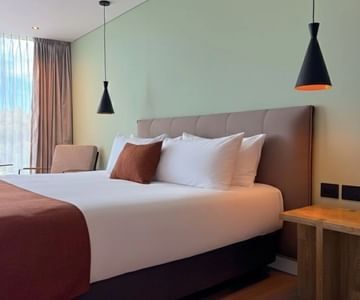 King bed with brown headboard between black pendant lamp beside armchair near window inside Hotel B3 Sibelius