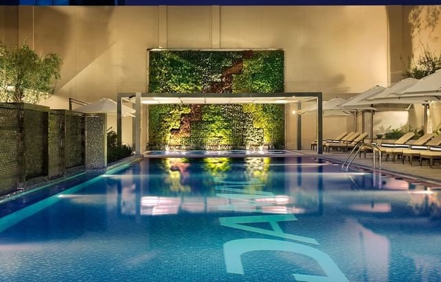 Large swimming pool beside comfy lounge chairs and a vibrant green wall backdrop at the premium DAMAC Maison Cour Jardin