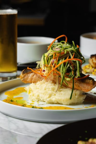 Piece of salmon on creamy mashed potatoes, topped with colorful shredded vegetables at Cypress & Oak Steakhouse, Frankfort