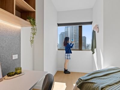 Woman taking a photo through a large window in a furnished room at UniLodge Brisbane City.