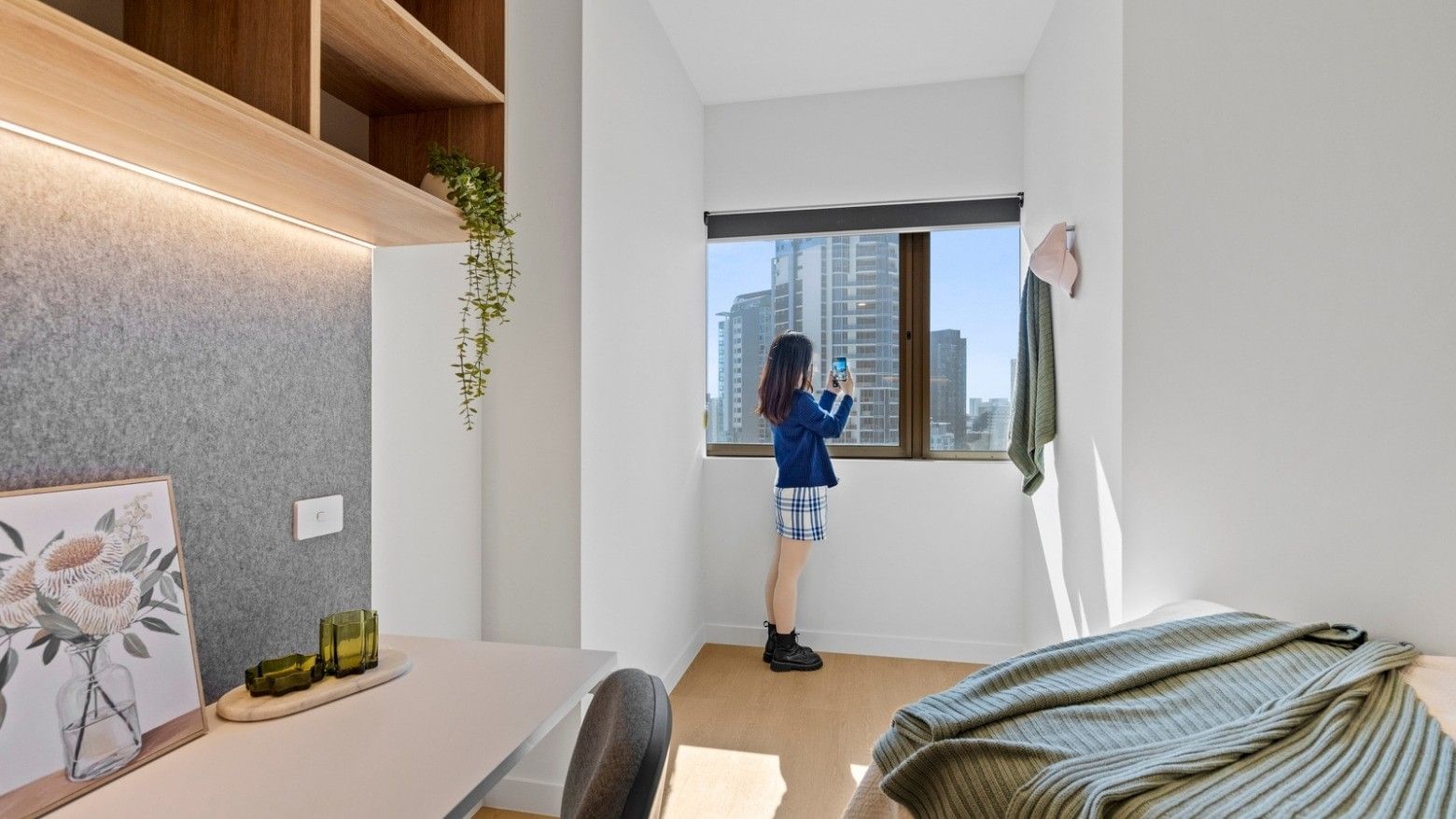Woman taking a photo through a large window in a furnished room at UniLodge Brisbane City.