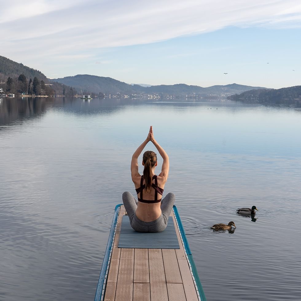 Woman doing yoga by the lake near Falkensteiner Hotels