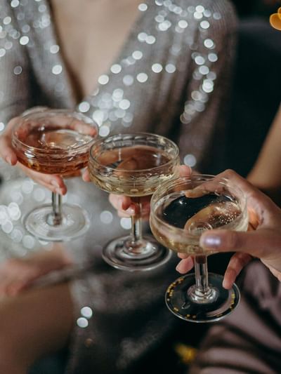 Guests toasting with champagne coupe glasses in elegant attire with sparkling lights in the background