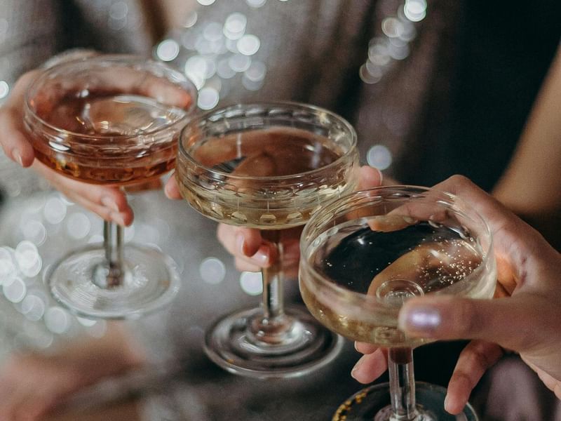 Guests toasting with champagne coupe glasses in elegant attire with sparkling lights in the background