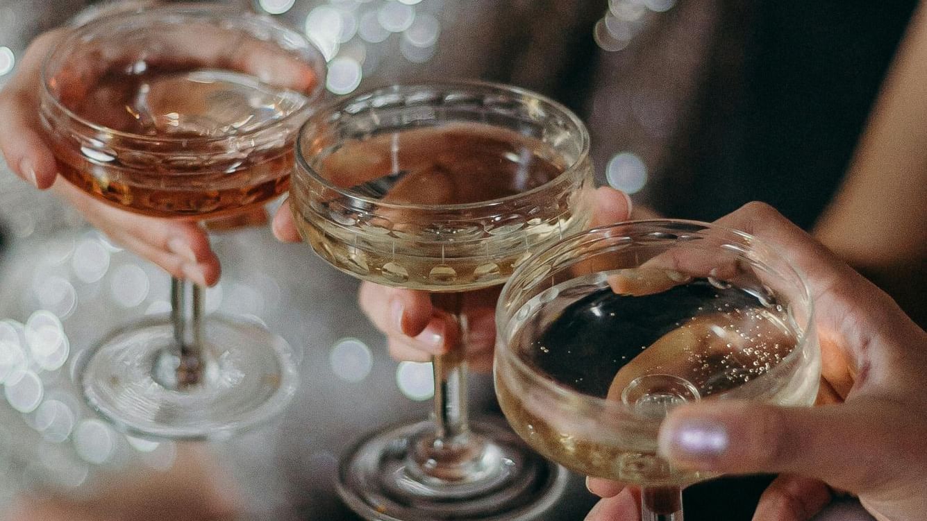 Guests toasting with champagne coupe glasses in elegant attire with sparkling lights in the background