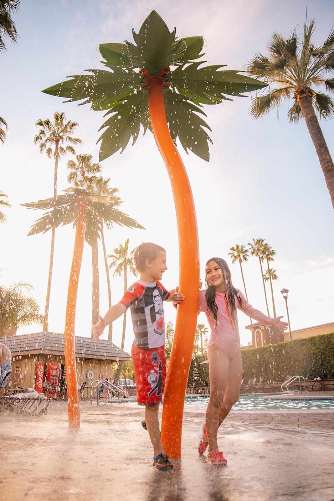 Two children playing near a palm tree water feature at a pool