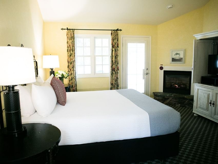 A cozy hotel room with a large bed, fireplace, TV, and window with curtains.
