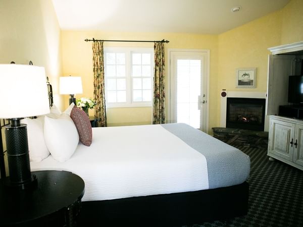 A cozy hotel room with a large bed, fireplace, TV, and window with curtains.