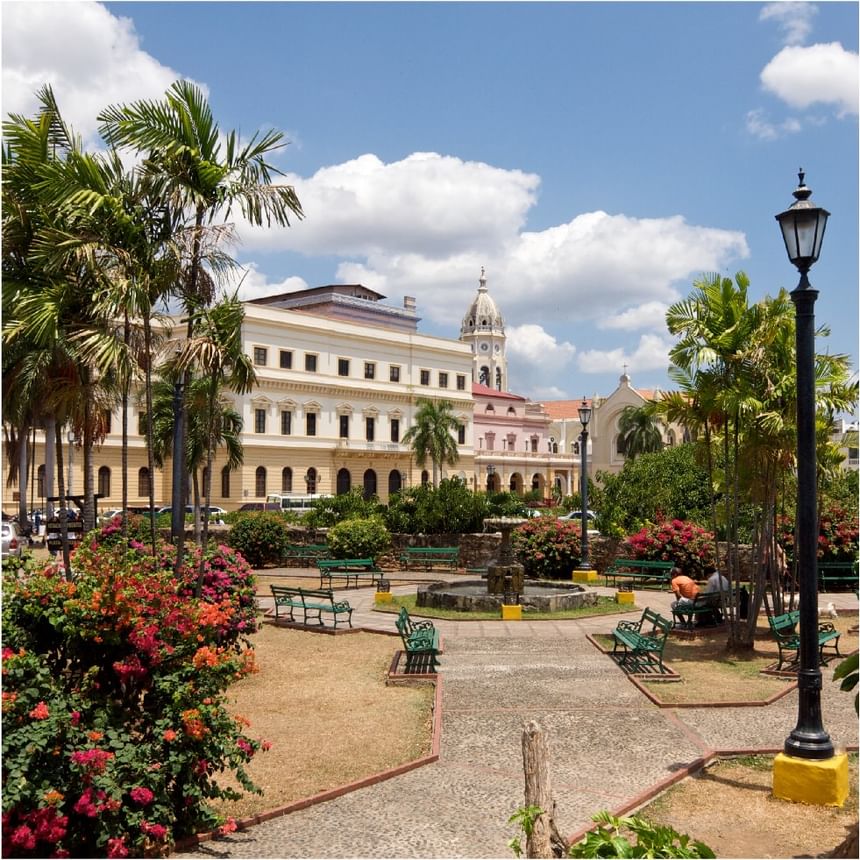 Plaza con bancos verdes, fuente de piedra, flores y edificios coloniales cerca de Megapolis Hotel Panama