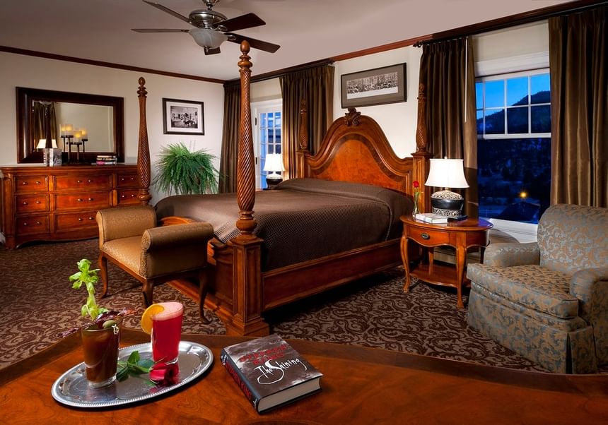 Bed room with a comfy large bed, patterned chair and a table with cocktails served on it at The Stanley Hotel