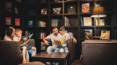 Family of four reading books in a cozy room with bookshelves and a coffee table.