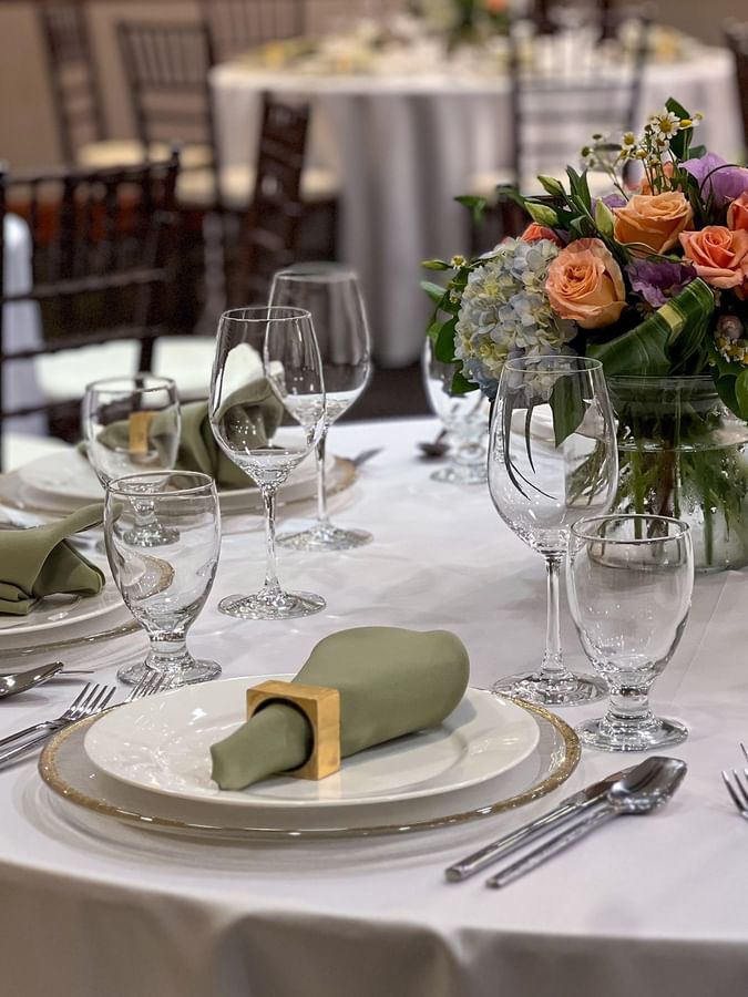 Banquet table setting featuring white plates, green napkins, and a floral centerpiece in Sasquatch Room A at Warwick Seattle