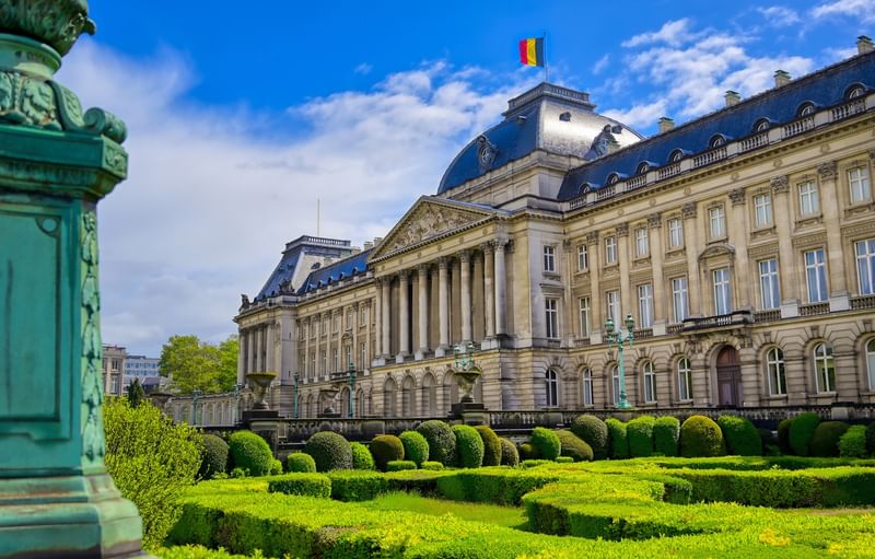 Elegant building with Belgian flag and blue domes, surrounded by manicured gardens at Hotel Barsey by Warwick 