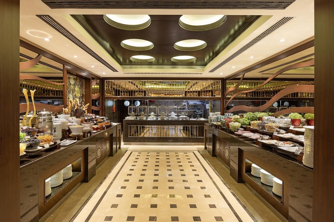 Plates of food on a tiled floor in a large buffet area under recessed lights at Titanic City Taksim