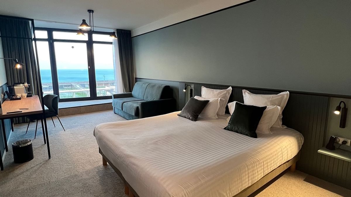 Chambre d'hôtel avec lit king size, canapé, bureau et vue sur l'océan.