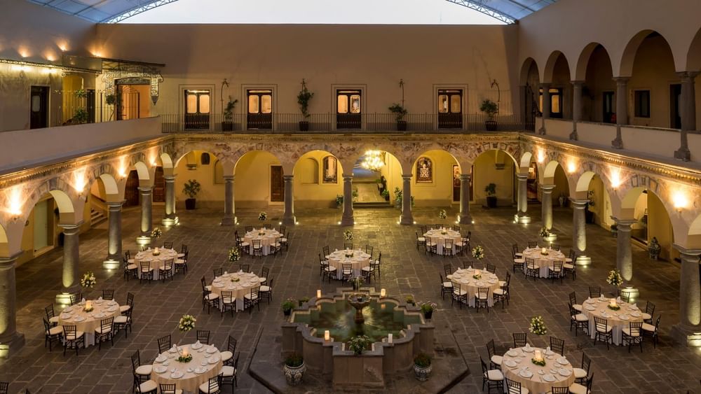 Overhead view of round banquet tables in a historic courtyard with stone pillars in Patio Novicias at Quinta Real Puebla