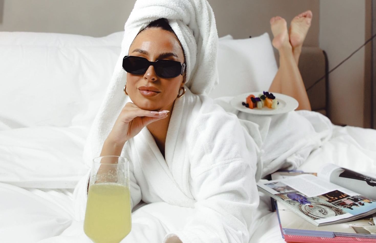 Lady posing for a picture in a bathrobe and having juice on the bed at The Londoner