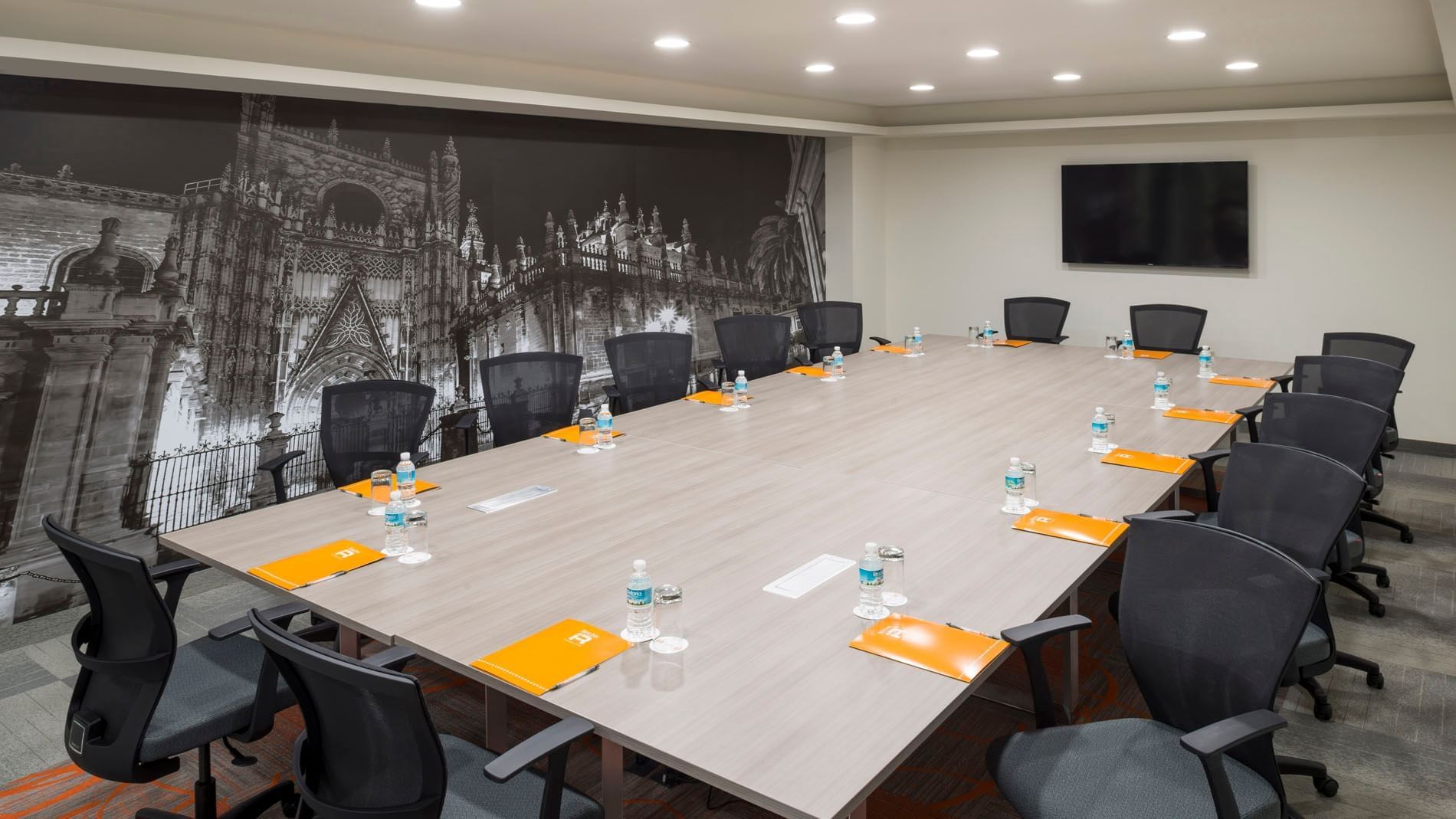 Detroit boardroom with a large wooden table, black chairs, and a cathedral wall mural design at Real Inn Celaya