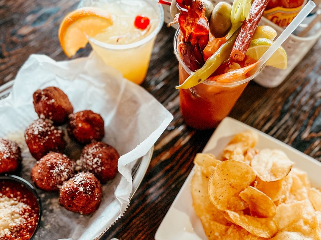 Plate of chips, basket of fried balls, and two drinks on a wooden table.