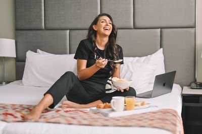 Lady enjoying a meal on the bed, Nesuto Parramatta Sydney Hotel